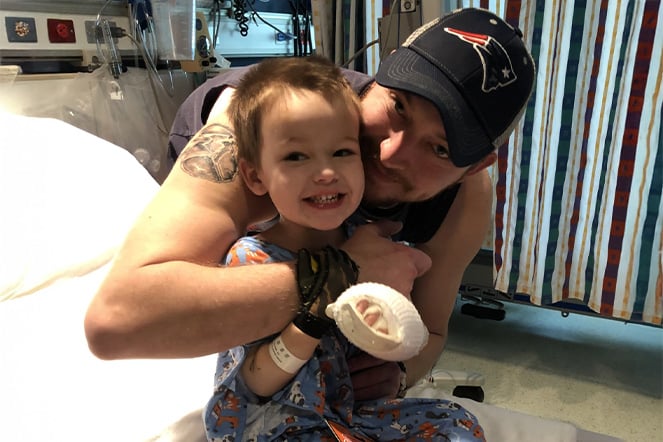 a father holding a smiling child with hand wraps in a hospital room