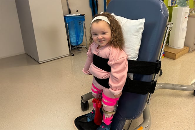 a smiling child standing while being held in an assistive chair
