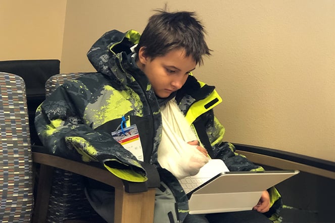 a child with his arm in a sling playing with an computer tablet