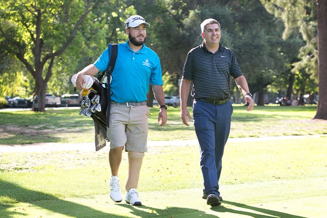 a man with a prosthetic leg walking with another man on a golf course