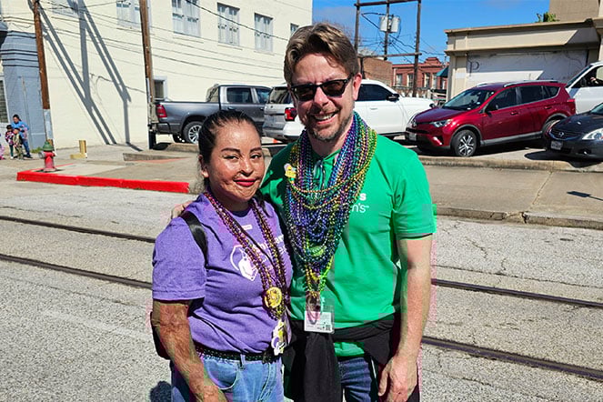 a child with burn scars and multiple bead necklaces smiles next to an adult wearing multiple bead necklaces