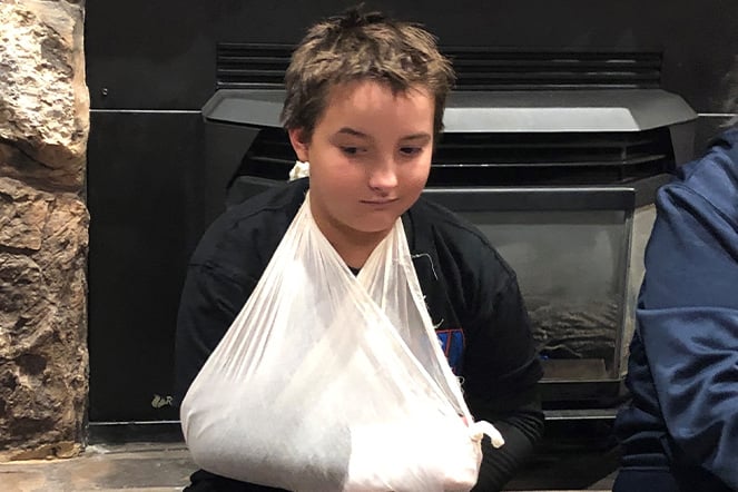 a child withi his arm in a sling sitting in front of a fireplace