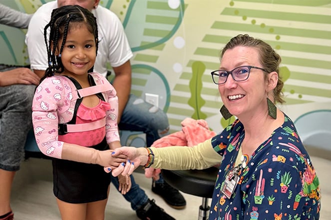 a woman shaking the hand of a child with a prosthetic arm