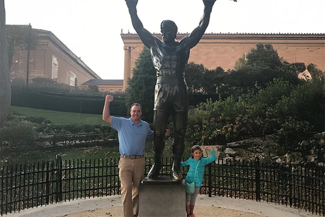 a man and a young child raising their arms with a statue of a boxer