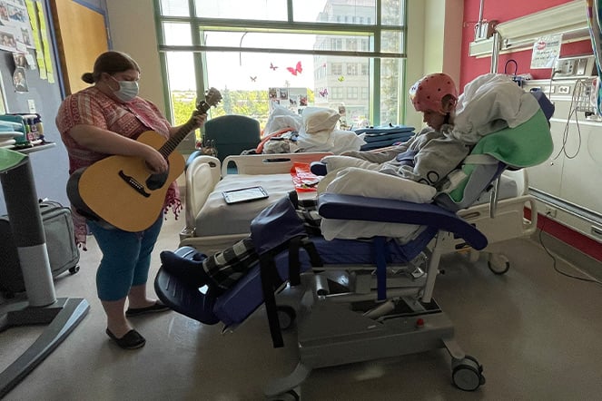 a guitarist performing for a child in a hospital bed