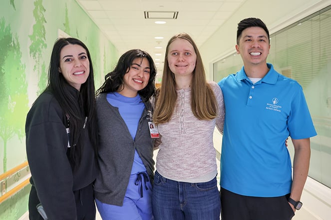 three adults standing with a smiling teenager
