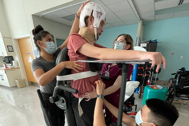 four adults assisting a standing child