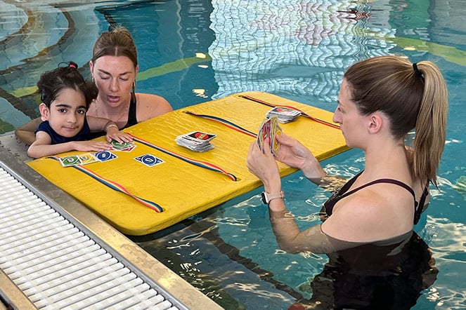 two women helping a child float in a pool