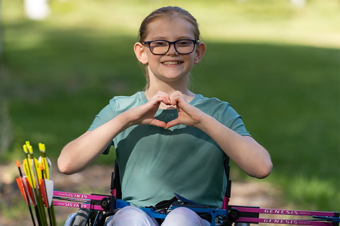 a patient in a wheelchair with archery bows making a heart with her hands