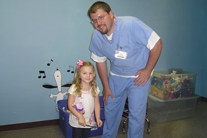 a child standing next to an adult in hospital scrubs in front of bins of toys