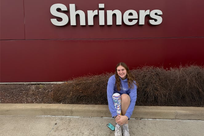 a child with a prosthetic leg sitting under a sign that reads "Shriners"