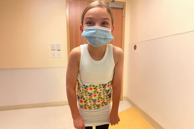 a smiling child wearing a mask and a scoliosis brace