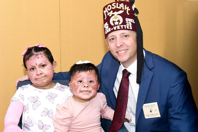 a man wearing a suit and fez smiling with two child burn care patients