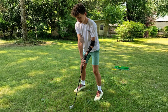 a teenager preparing to golf with their arm prosthetic adapted to hold a club