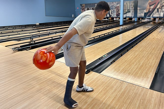 a teen with a leg case preparing to roll a bowling ball