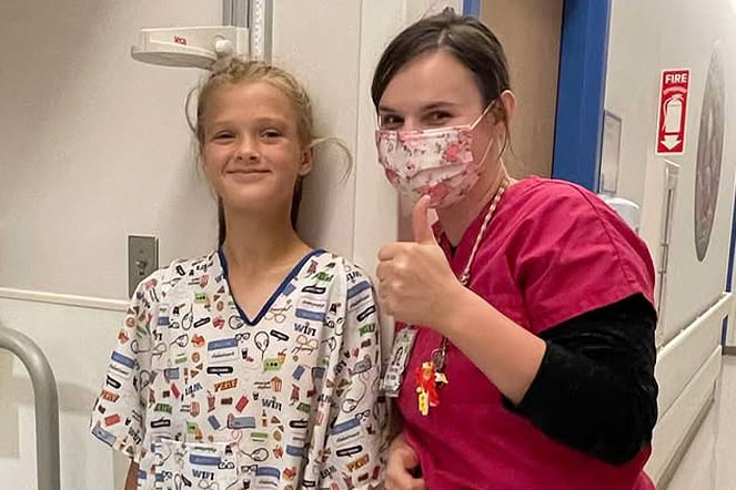 a nurse wearing a mask giving a thumbs up next to a smiling child