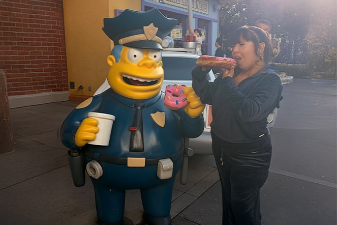 a teenager eating a large donut next to a cartoon character statue