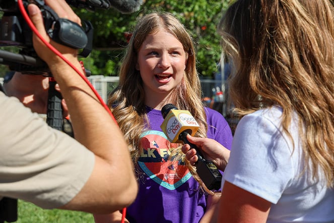 a child speaking into a microphone during an interview with a woman and a man holding a camera