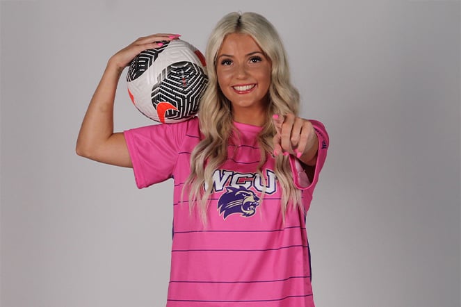 a teenage girl holding a soccer ball on her shoulder