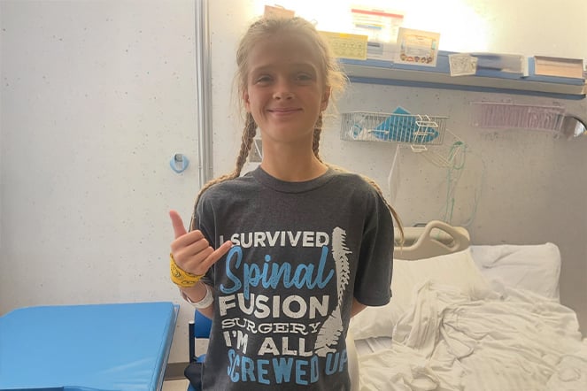 a child wearing a shirt that reads "I survived spinal fusion surgery I'm all screwed up"