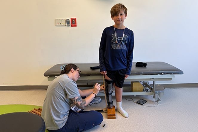 a child standing while a woman adjust his prosthetic leg