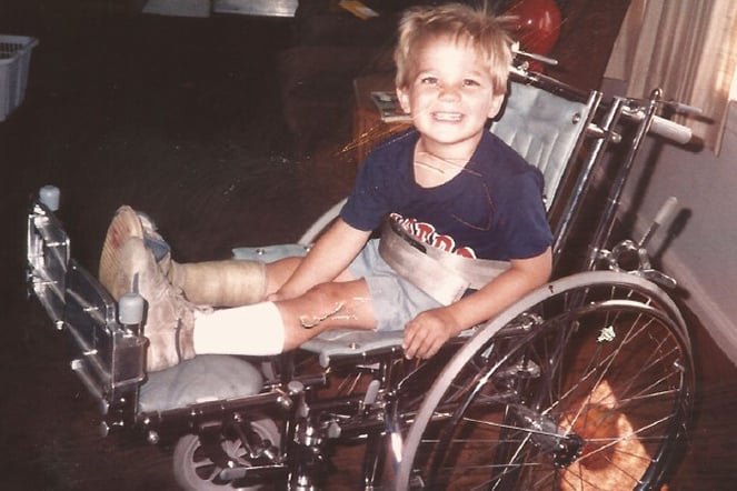 a vintage photo of a child in a wheelchair with a cast on his leg