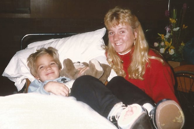 an aged photo of a woman kneeling next to a smiling boy in a bed