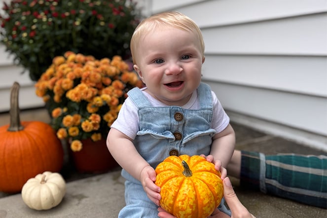 a smiling baby holding a small pumpkin