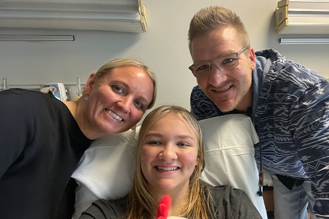 two parents surrounding a smiling child in a hospital bed