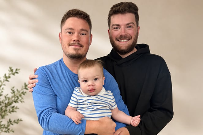two men smiling while holding a baby