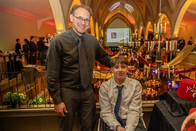 a man standing next to a teen in a wheelchair in a large ballroom