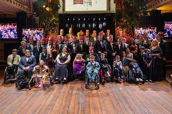 a large group photo of men in fezzes and children in wheelchairs at a gala