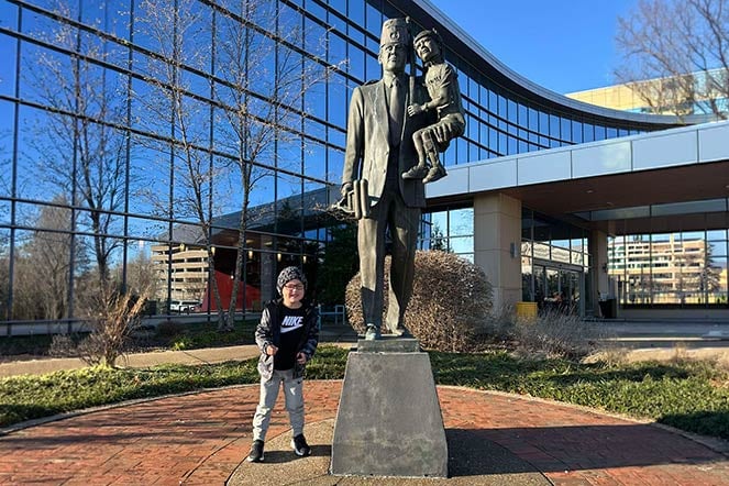 orthopedic patient stands outside next to statue