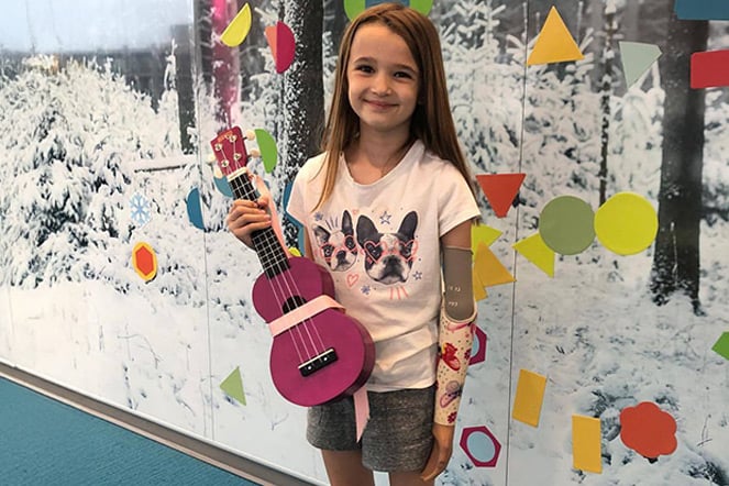 a child with a prosthetic arm holding a ukulele