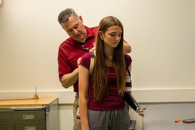 an adult adjusting a prosthetic arm on a child