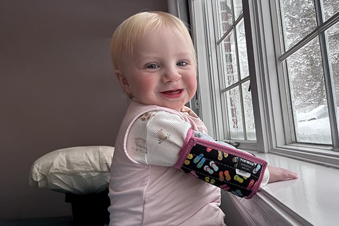 a smiling child with and arm brace standing at a window