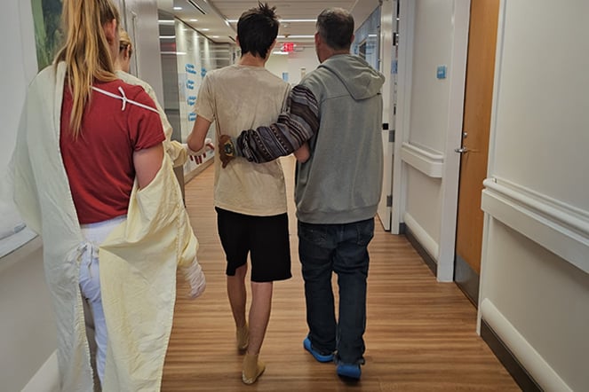 a father and son walking in a hallway of a hospital with staff