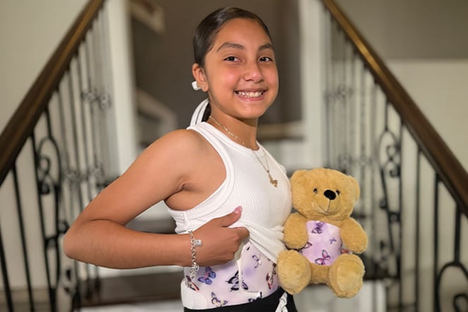 a childing proudly displaying her scoliosis brace with a teddy bear in a matching brace