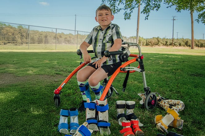 a child sitting in a walker in front of a collection of leg braces