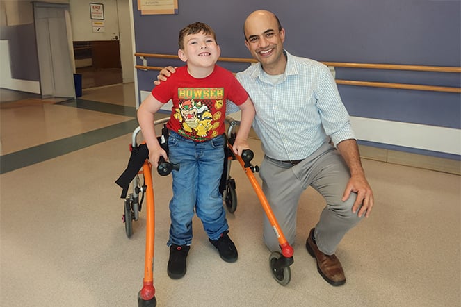 a child in a walker smiling with a couching adult
