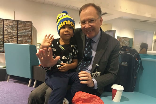 a child and a man sitting in a hospital lobby waving their hands