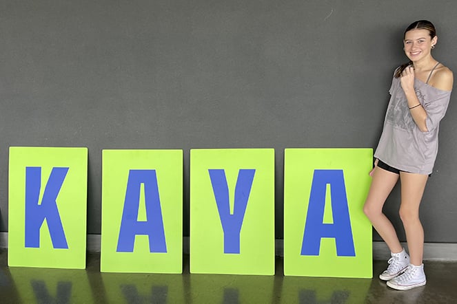 a childing standing next to colorful signs that spell out "KAYA"
