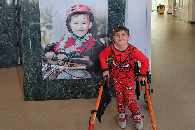 a child in a walker smiling in front of a photo of himself
