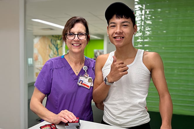 a woman in hospital scrubs holds an Uno card deck with a child in a tank top shirt