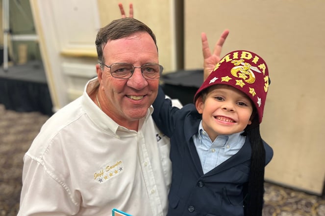 a child wearing a fez taking a silly photo with a kneeling man