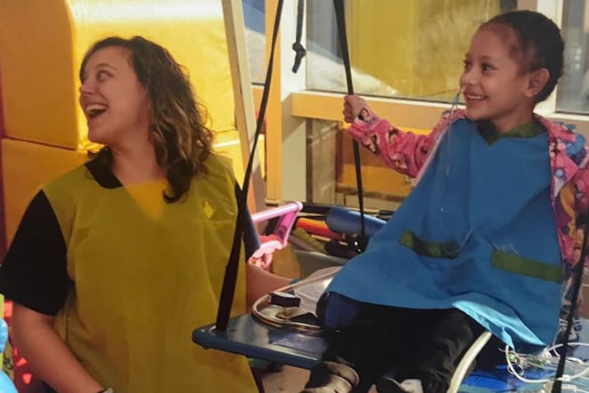 a woman wearing a smock laughing with a child in a swing