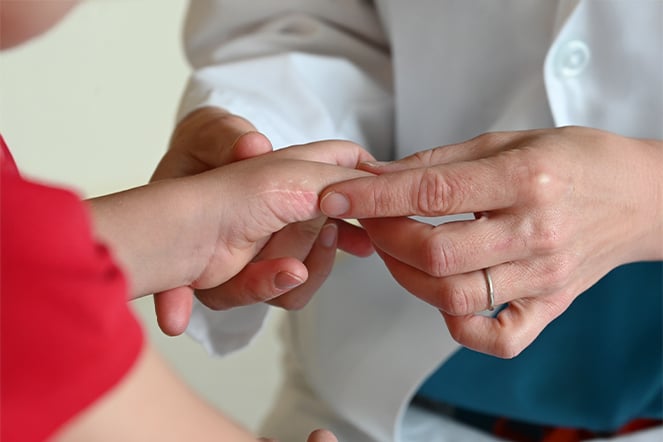 a doctor's hands examining the thumb on a child's hand 