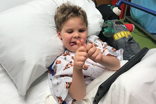 a smiling child in a hospital bed putting this hands together at the thumb