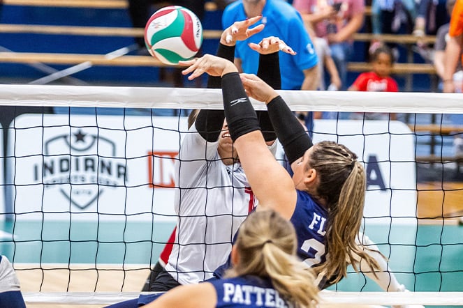 a volleyball player spikes the ball over the net in front of an opposing player