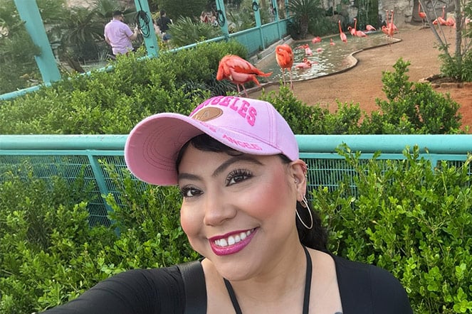A person takes a selfie in front of a flamingo habitat at a zoo or wildlife park.